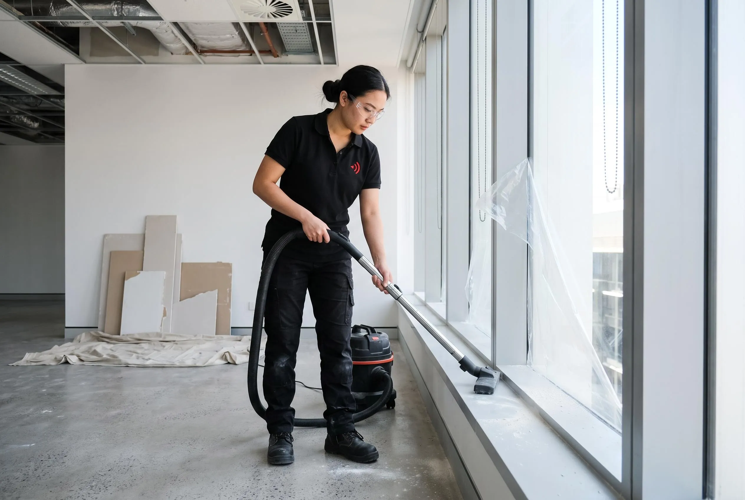 Cleaner vacuuming construction dust off a window sill in a newly completed office fit-out