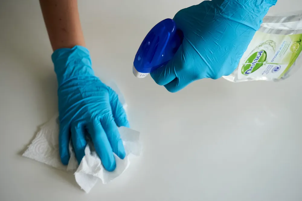 Gloved hand wiping down a surface with cleaning spray